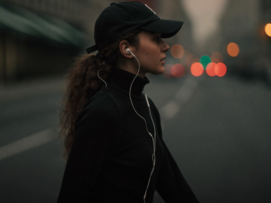 Woman walking city street wearing wired earbuds